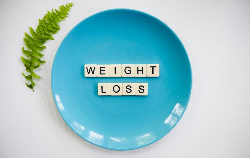 pexels-photo-2377045-2377045 A blue plate with 'weight loss' tiles and a fern leaf on white background.