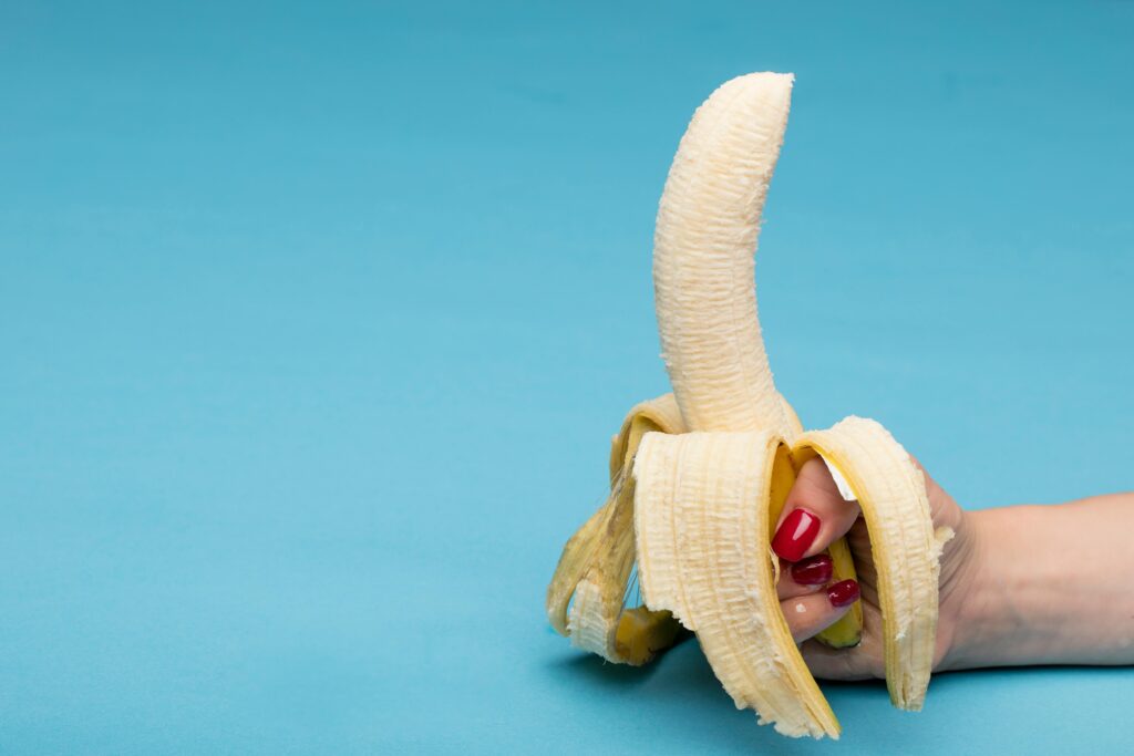 pexels-photo-5750196-5750196 Peeled banana held by hand against a blue background, offering conceptual visual appeal.