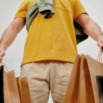 A young adult carrying paper shopping bags symbolizes retail therapy and consumerism indoors.